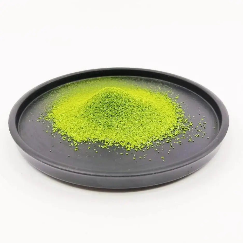 Vibrant green matcha powder piled on a black ceramic dish, showcasing premium Japanese tea quality.