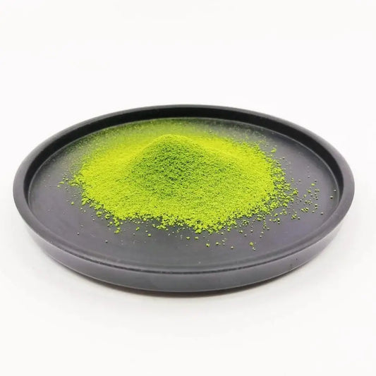 Vibrant green Japanese matcha tea powder on a black plate, isolated on white background.