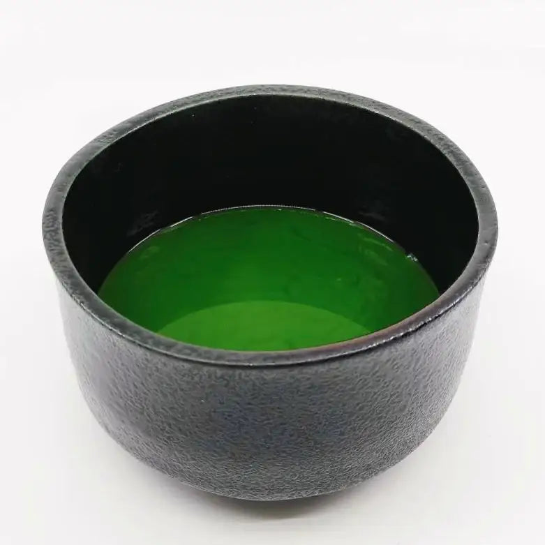 Black textured tea bowl with vibrant green matcha, showcasing Japanese teaware craftsmanship