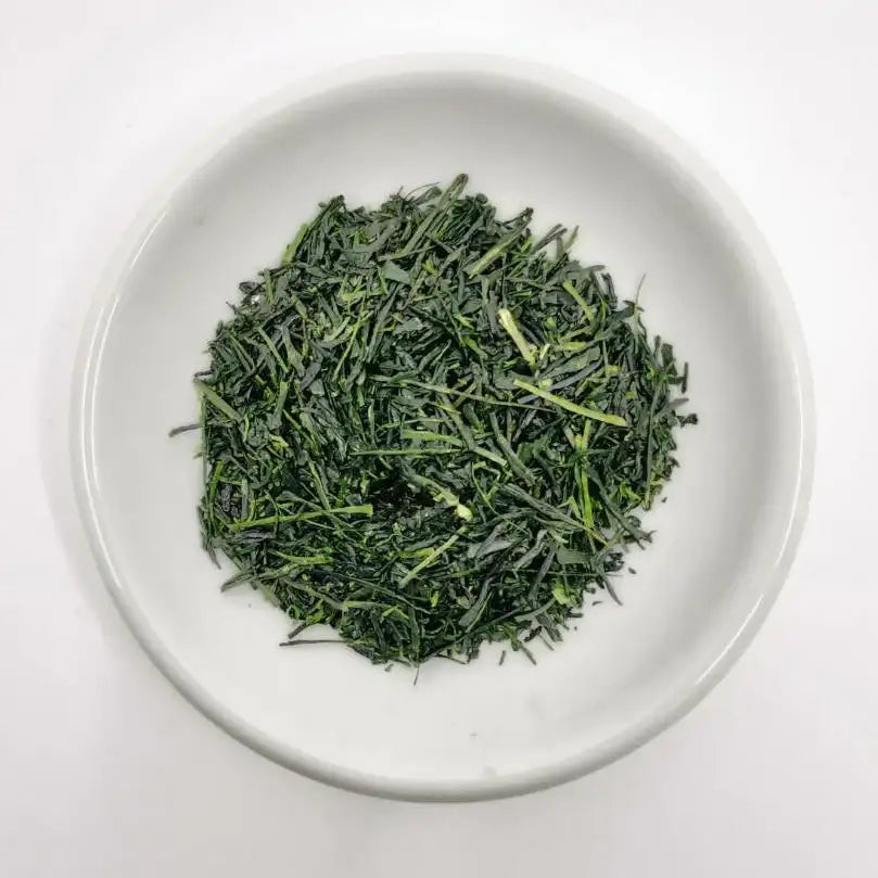 Fresh Japanese green tea leaves in a white ceramic bowl, showcasing vibrant color and texture