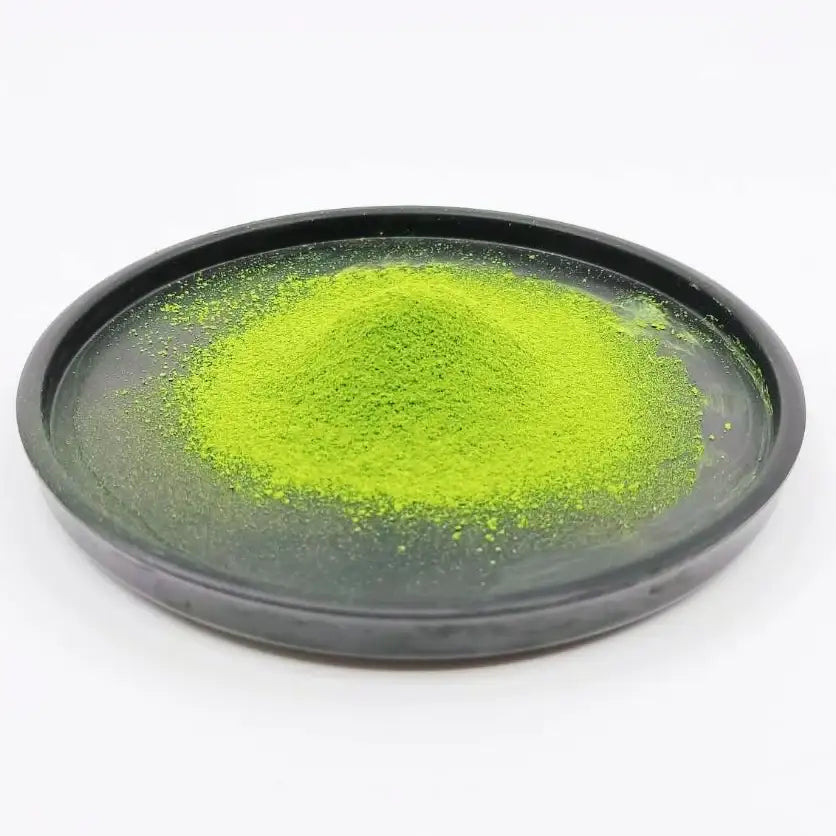 Vibrant green matcha powder piled in a dark ceramic dish, showcasing premium Japanese tea quality.