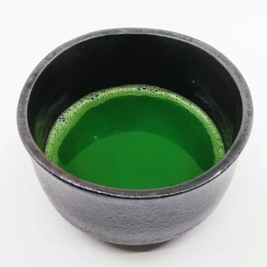 Vibrant green matcha tea in a textured black ceramic bowl, showcasing authentic Japanese tea culture.